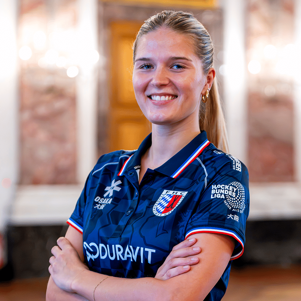 Eine lächelnde Hockeyspielerin im blauen Trikot des FHC vor verschwommenem Hintergrund, repräsentativ für Hockey in Mannheim und den MHC.