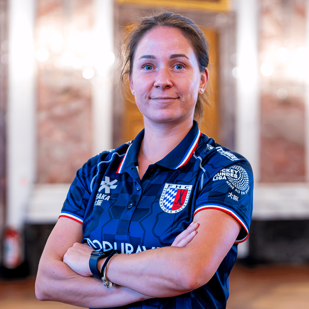 Eine Sportlerin des Feudenheimer Hockeyclubs mit verschränkten Armen in ihrem blauen Trikot, repräsentativ für Hockey in Mannheim und den MHC.