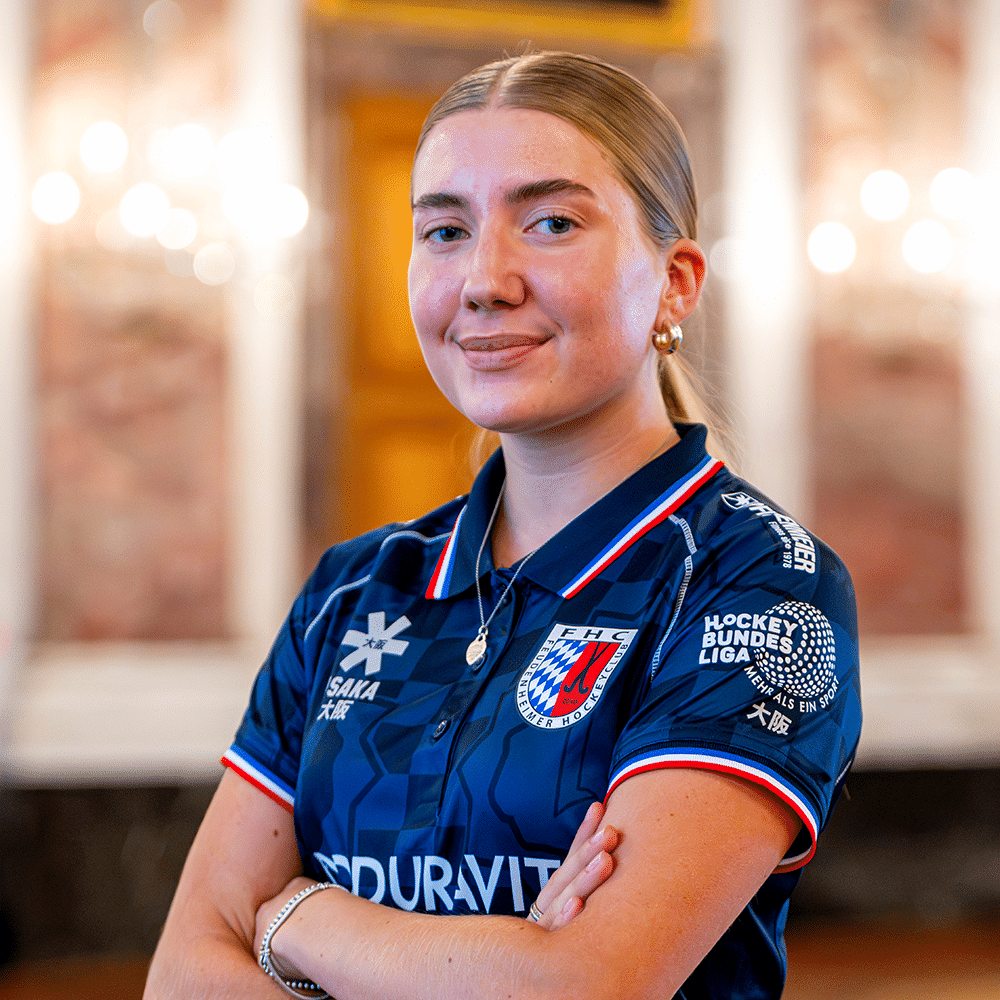 Eine junge Spielerin des Feudenheimer Hockeyclubs lächelt in die Kamera. Sie trägt ein blaues Trikot, ähnlich wie beim MHC und Hockey in Mannheim.