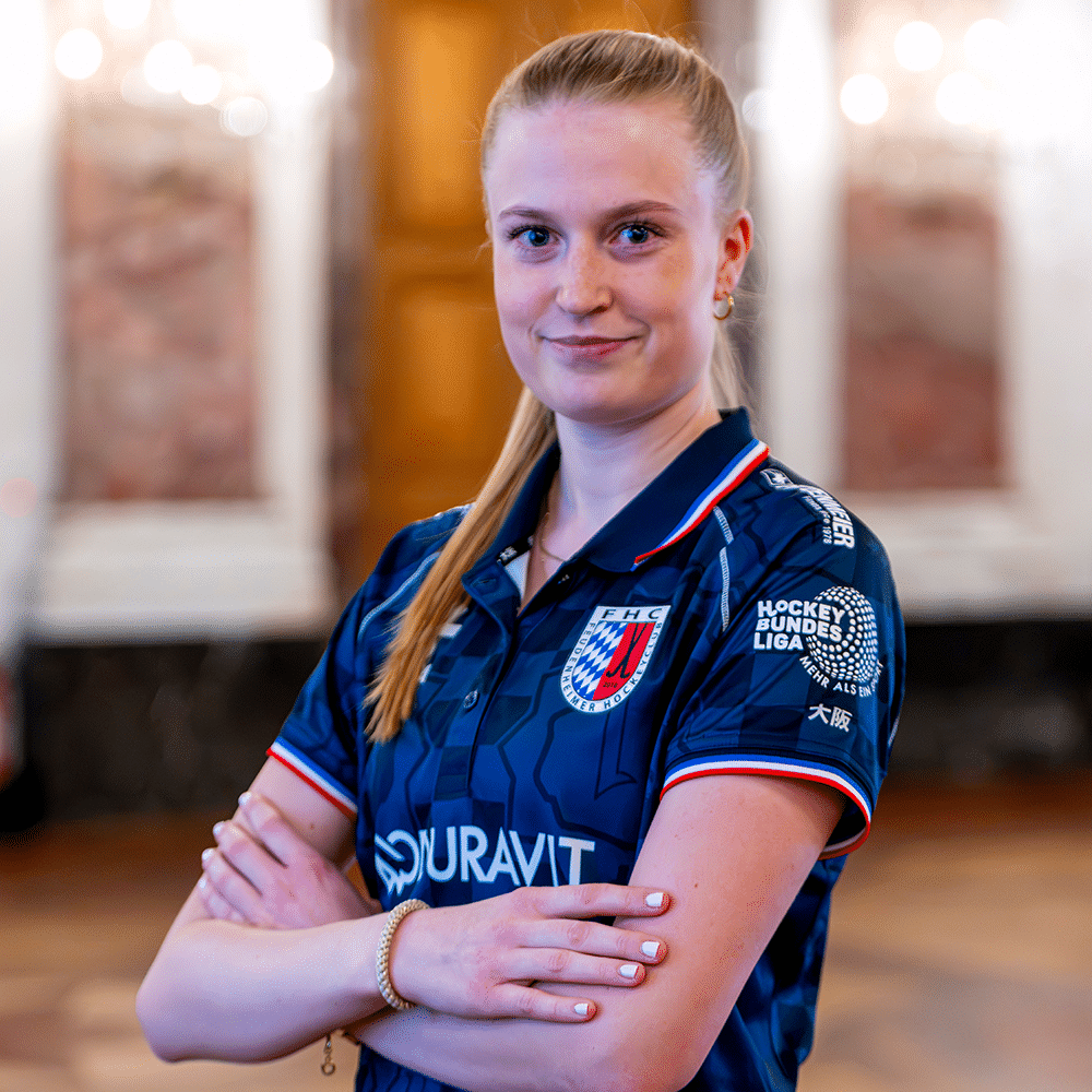 Eine junge Hockeyspielerin in einem blauen Trikot vom Mannheimer Hockeyclub posiert selbstbewusst für ein Foto. Hockey in Mannheim steht für Qualität.